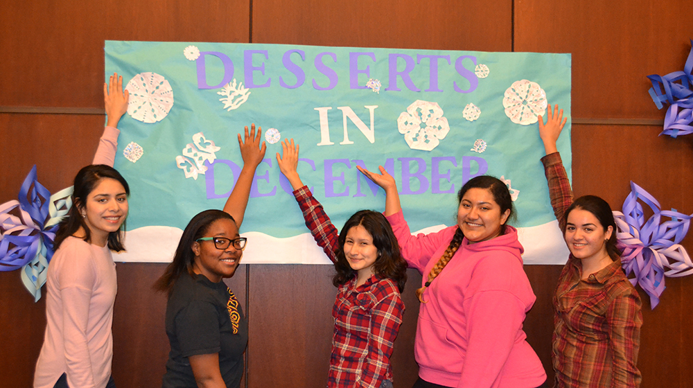 five women with their hands on a Dessert in December 2013 banner smiling